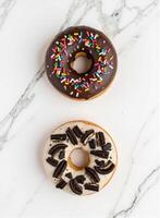 Two donuts enjoyment with chocolate and sprinkles on a marble surface photo