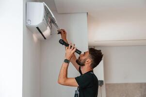 Using screwdriver ,and flashlight., Man repairs an air conditioner indoors at home photo