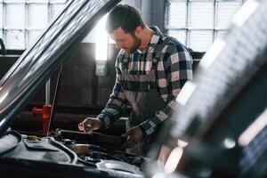 Hood of the car is opened. Using tablet. Man in uniform is working in the auto salon photo