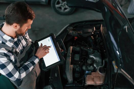 With tablet, in hands. Man in uniform is, working in the auto salon photo