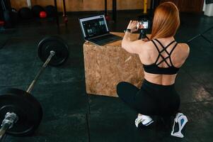 Setting ,up smartphone on, the tripod. Beautiful strong woman is in the gym photo
