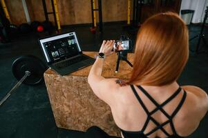 Setting up smartphone ,on ,the tripod. Beautiful strong woman is in the gym photo