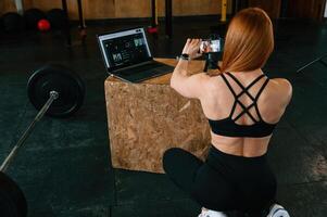 Setting up, smartphone, on the tripod. Beautiful strong woman is in the gym photo