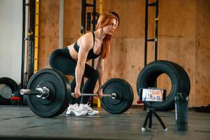 With barbell. Shooting by smartphone. Beautiful strong woman is in the gym photo
