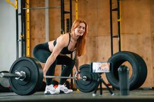 Side view,, with barbell. Smartphone on tripod capturing . Beautiful strong woman is in the gym photo