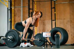 Side, view, with barbell. Smartphone on tripod capturing . Beautiful strong woman is in the gym photo