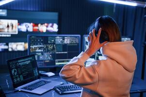 Wearing, headphones. Young professional female hacker is indoors by computer with lot of information on displays photo
