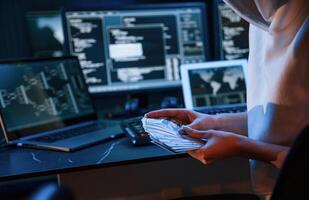 With, currency, in hands. Young professional female hacker is indoors by computer with lot of information on displays photo