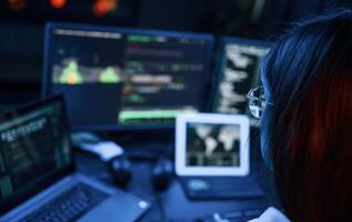 Young ,,professional female hacker is indoors by computer with lot of information on displays photo