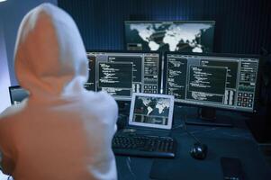 Young, professional female hacker, is indoors by computer with lot of information on displays photo