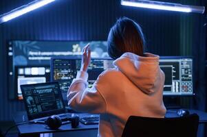 Looking, at screens. Young professional female hacker is indoors by computer with lot of information on displays photo