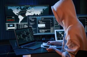 With, currency in hands. Young professional female hacker is indoors by computer with lot of information on displays photo