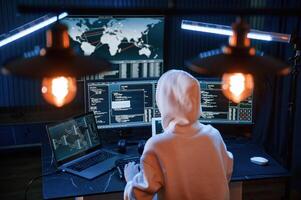 Sitting, in white hoodie. Young professional female, hacker is indoors by computer with lot of information on displays photo