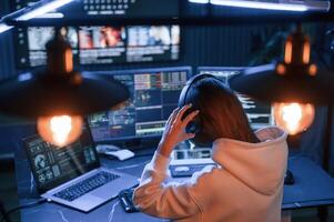 Wearing ,headphones.. Young professional female hacker is indoors by computer with lot of information on displays photo