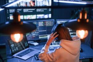 Wearing headphones.. Young,, professional female hacker is indoors by computer with lot of information on displays photo