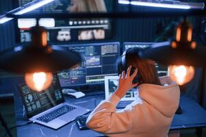 Wearing headphones.. Young ,professional female hacker is indoors by computer with lot of information on displays photo
