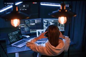 Looking, at screens. Young professional, female hacker is indoors by computer with lot of information on displays photo