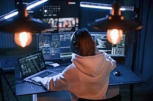 Artificial, lighting. Young professional female, hacker is indoors by computer with lot of information on displays photo