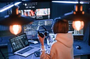 Artificial lighting,. Young, professional ,female hacker is indoors by computer with lot of information on displays photo