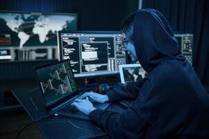 Black colored hoodie. Young professional female hacker is indoors by computer with lot of information on displays. photo