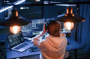 Artificial, lighting.. Young professional female hacker is indoors by computer with lot of information on displays photo