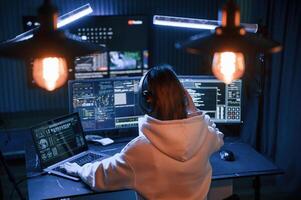 Looking ,at ,screens. Young professional female hacker is indoors by computer with lot of information on displays photo