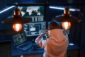 View, from behind. Young professional female hacker, is indoors by computer with lot of information on displays photo