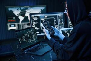 Black colored hoodie. Young professional ,female hacker is indoors by computer with lot of information on displays photo