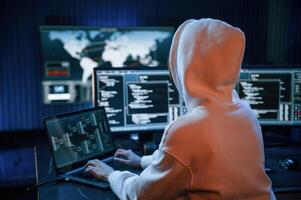 In white hoodie. Young ,professional female hacker is indoors by computer with lot of information on displays photo