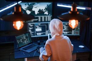 Sitting in white hoodie... Young professional female ,hacker is indoors by computer with lot of information on displays photo