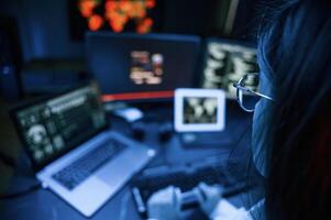 Young professional female hacker is indoors by computer with lot of information on displays photo