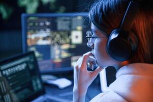 Focused on work. Young professional female hacker is indoors by computer with lot of information on ,displays photo