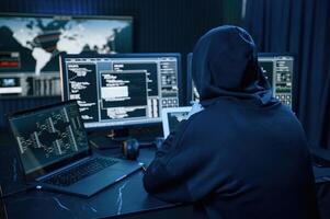 Black colored hoodie. Young ,professional female, hacker is indoors by computer with lot of information on displays photo