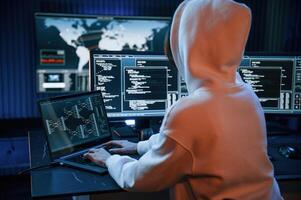 In white hoodie.. Young professional female hacker is indoors by computer with lot of information on displays photo