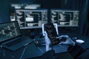 Holding smartphone with code. Young ,professional ,female hacker is indoors by computer with lot of information on displays photo