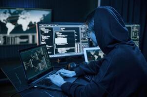 Black ,colored ,hoodie. Young professional female hacker is indoors by computer with lot of information on displays photo
