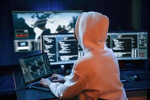 In ,white hoodie. Young professional female hacker is indoors by computer with lot of information on displays photo