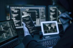 Holding smartphone ,with code. .Young professional female hacker is indoors by computer with lot of information on displays photo