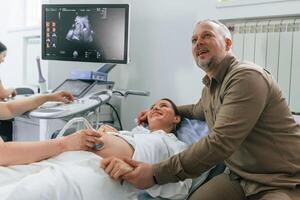 Husband is supporting his wife. .Pregnant ,woman is lying down in the hospital, doctor does ultrasound photo