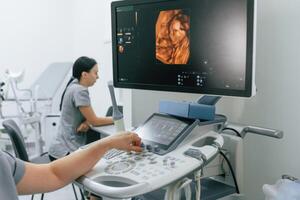 Nurse is working in the clinic, doing an ultrasound scan of the belly of a pregnant woman. Display with little baby photo