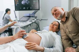 Husband is ,supporting his wife. Pregnant woman is lying down in the hospital, doctor does ultrasound photo