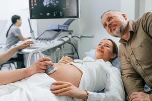 Husband is supporting his, wife.. Pregnant woman is lying down in the hospital, doctor does ultrasound photo