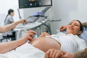 Smiling,, medical procedure. Pregnant woman is lying down in the hospital, doctor does ultrasound photo