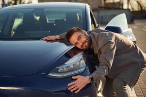 Embracing ,the automobile.. Man is standing near his electric car outdoors photo