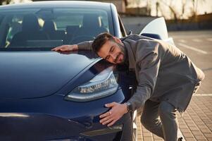 Embracing, the automobile. Man is standing near his electric car outdoors photo