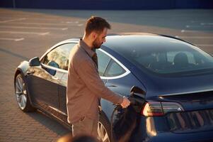 Time to charge the automobile. ,Man is standing near his electric car outdoors photo