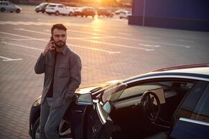 Evening time. ,Beautiful sunlight,. Man is standing near his electric car outdoors photo