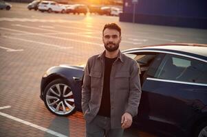 Sunny background. Man is standing, near ,his electric car outdoors photo