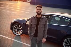 Sunny background.,, Man is standing near his electric car outdoors photo