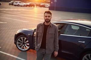 Sunny, background. Man is standing near, his electric car outdoors photo